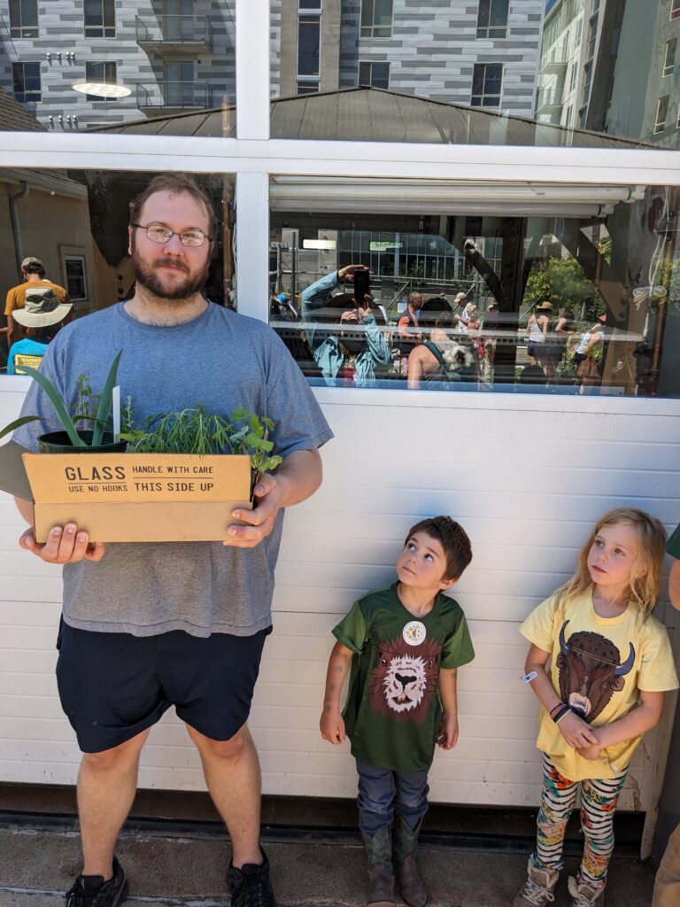 Father with a box of Colorado native plants from the swap with his young children looking on with curiousity.